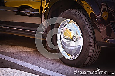 Details of a Dark Shiny Car with Bright Mirror Chrome Wheel Cover and Reflection of another Yellow Car in It Stock Photo