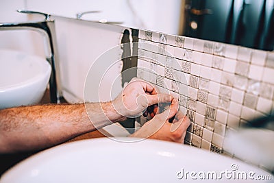 Details of industrial worker applying mosaic ceramic pattern tiles on bathroom shower area Stock Photo