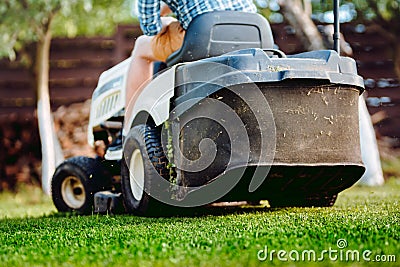 Details of landscaping and gardening. Worker riding industrial lawnmower Stock Photo