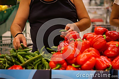 Details of a man choosing hot green peppers sweet red peppers also on the shelf on the fruits and vegetables aisle in a store Stock Photo