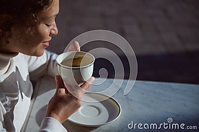 A white porcelain cup with coffee drink in hands of a smiling woman telling fortunes on coffee grounds. People. Leisure Stock Photo