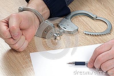 A detainee at the police station. One hand is cuffed, the other is unbuttoned, and there is a pen in his hand for writing Stock Photo
