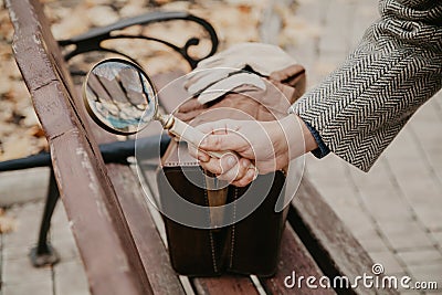 Detective hand holds magnifier over wooden park bench Stock Photo