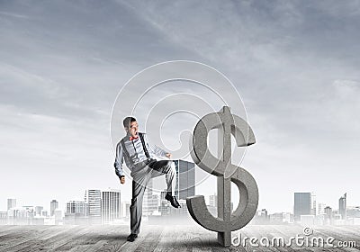 Determined banker man against modern cityscape breaking dollar cement figure Stock Photo