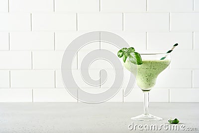 Detox green vegetable juice or smoothie garnished with leaf of fresh basil in coctail glass on light gray slate, stone or concrete Stock Photo