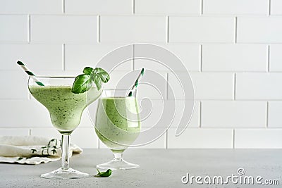 Detox green vegetable juice or smoothie garnished with leaf of fresh basil in coctail glass on light gray slate, stone or concrete Stock Photo