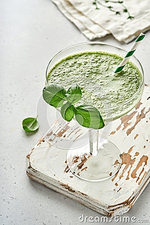 Detox green vegetable juice or smoothie garnished with leaf of fresh basil in coctail glass on light gray slate, stone or concrete Stock Photo