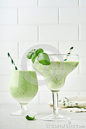 Detox green vegetable juice or smoothie garnished with leaf of fresh basil in coctail glass on light gray slate, stone or concrete Stock Photo