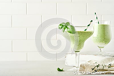 Detox green vegetable juice or smoothie garnished with leaf of fresh basil in coctail glass on light gray slate, stone or concrete Stock Photo