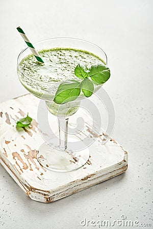 Detox green vegetable juice or smoothie garnished with leaf of fresh basil in coctail glass on light gray slate, stone or concrete Stock Photo