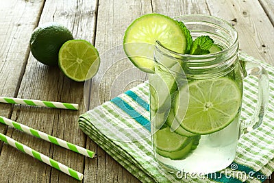 Detox water with lime and cucumbers in jar against wood Stock Photo