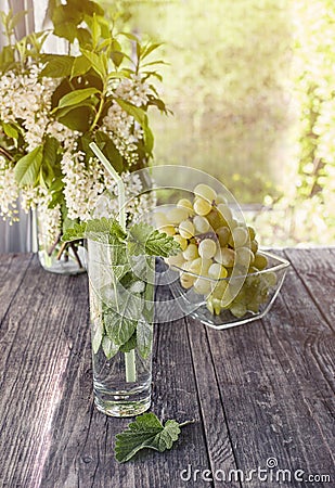 Detox water mint, grape juice and ice in a glass on a background of a bouquet of cherries and grapes on a Sunny day. The vertical Stock Photo