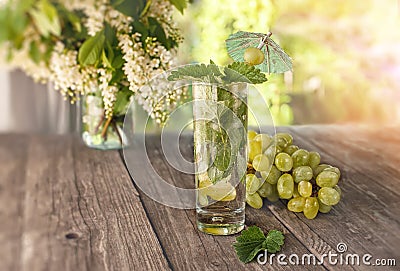 Detox water mint, grape juice and ice in a glass on a background of a bouquet of cherry and grapes in a Sunny day. The horizontal Stock Photo