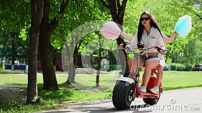Deux belles filles dans des shorts de denim montent en parc sur un scooter électrique pendant l'été banque de vidéos Deux belles filles dans des shorts de denim montent en parc sur un scooter électrique pendant l'été banque de vidéos