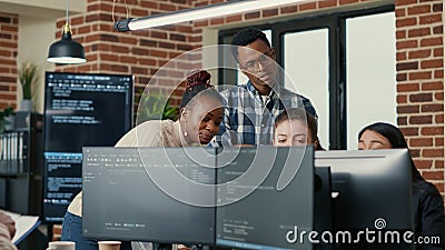 Developers brainstorming ideas looking at code on computer screens asking feedback from senior developer Stock Photo