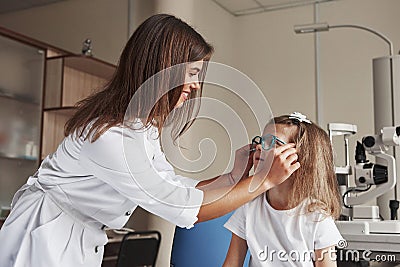 These device are suitable for you. Little girl tries new blue glasses in ophthalmologic office with female doctor Stock Photo
