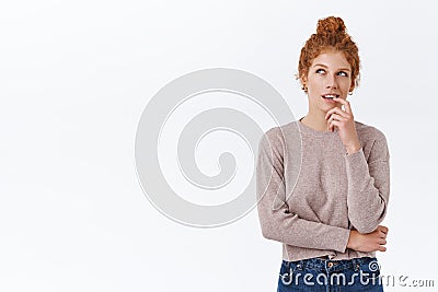 Devious, creative and pensive cute redhead woman with curly hair combed in bun, biting finger and looking up thoughtful Stock Photo