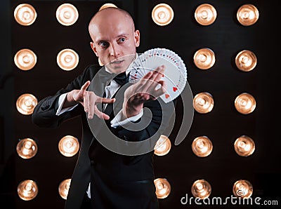 Dexterity of hands. Magician in black suit and with playing cards standing in the room with special lighting at Stock Photo