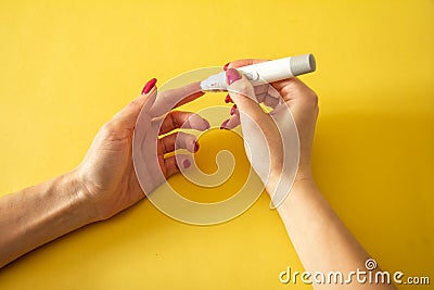 Diabet. Medical equipment. Medical concept. Close up of woman hands on yellow background using lancet on finger to check blood Stock Photo