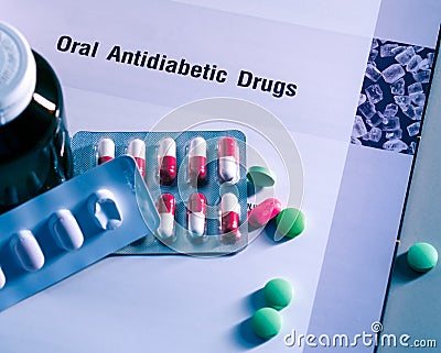 Diabetes drugs in packs and and medicine bottle placed on textbook. Green tablets and pink-white capsule pills. Diabetes mellitus Stock Photo