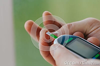 Diabetes, healthcare - close up of a man with a glucometer and a test strip checking blood sugar at home Stock Photo