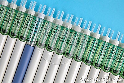 Diabetic insulin pens lined up on a blue background. One blue syringe in a row of many gray syringes Stock Photo