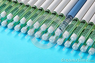 Diabetic insulin pens lined up on a blue background. One blue syringe in a row of many gray syringes Stock Photo