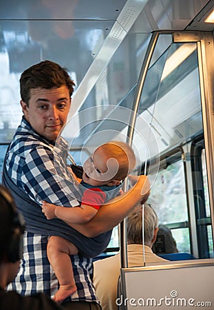 Young man and his little baby in sling in sunset lighting traveling in train car Editorial Stock Photo