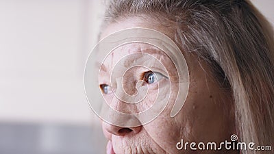Dichtbij de blauwe trieste ogen van de eenzame oudere vrouw die door het raam kijkt stock footage Dichtbij de blauwe trieste ogen van de eenzame oudere vrouw die door het raam kijkt stock footage