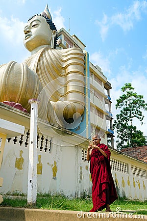 Dickwella, Sri Lanka, 04-15-2017: Buddhist monk holds mobile phone in hands of Buddhist temple on the background of Buddha statue Editorial Stock Photo