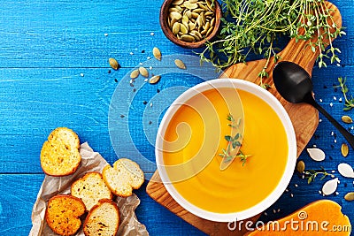 Diet autumn pumpkin or carrot cream soup in bowl served with seeds and crouton on blue rustic table top view Stock Photo