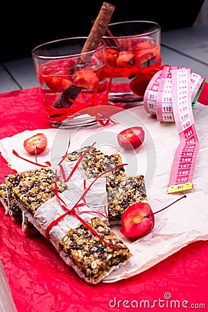 Diet muesli bars with detox apple cinnamon water and measuring tape on red pepper and wooden background Stock Photo