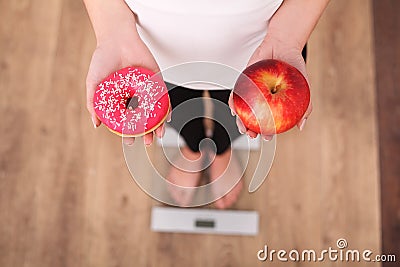 Diet. Woman Measuring Body Weight On Weighing Scale Holding Donut and apple. Sweets Are Unhealthy Junk Food. Dieting, Healthy Eati Stock Photo