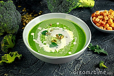 Dietary Broccoli smooth cream soup with sprinkle of sunflower seeds, parsley leaves and croutons on stone table. Stock Photo