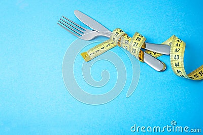 Dietary recipe dishes for breakfast, lunch or dinner. Fork and knife are wrapped in yellow measuring tape on blue background Stock Photo
