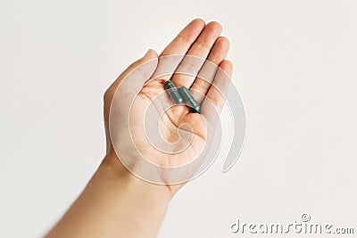 Dietary supplements. Hand holding spirulina capsules on white wall background. Morning vitamin nutrient pill. Health support and Stock Photo