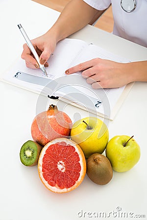 Dietician writing prescription with fruits on desk Stock Photo