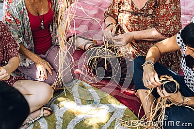 Different ages females weaving bascets on the craft workshop, sitting on a carpet on a flour. Stock Photo