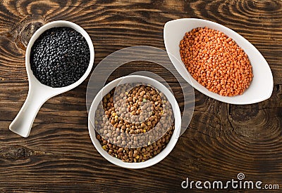 Different assorted lentils mix with red, brown and black beluga lentils in white bowls on brown wooden table background top view Stock Photo