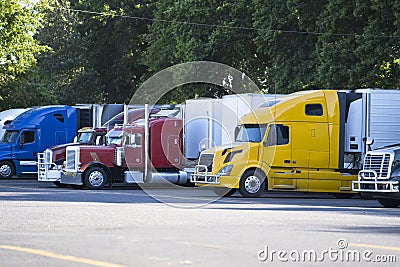 Different big rigs semi trucks with semi trailers standing in row on truck stop Stock Photo