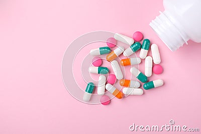 Different colorful drugs falling from the white bottle on pink background. Stock Photo