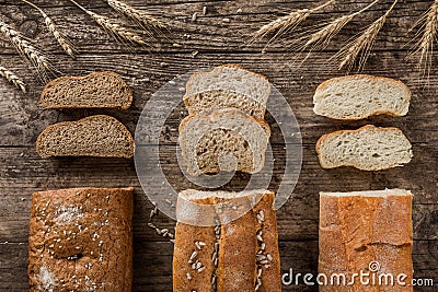 Different fresh bread and spikelets of wheat on rustic wooden background. Creative layout made of bread. Stock Photo