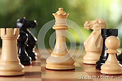 Different game pieces on chessboard against blurred background, closeup Stock Photo