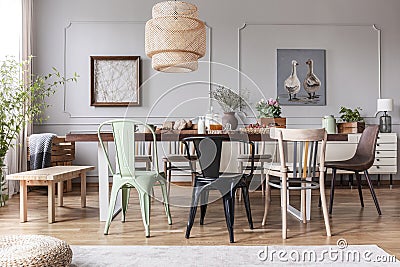 Different kid of chairs at table with flowers and food in rustic dining room interior with lamp and posters. Real photo Stock Photo