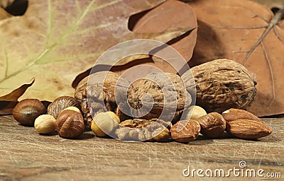 Different kinds of nuts hazelnuts, almonds, walnut on brown wooden table with autumn leaves. Vegetarian food Stock Photo