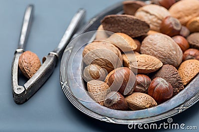 Different kinds of nuts in shell, hazelnut, walnut, almond and brazil nuts on plate with nut cracker, horizontal Stock Photo