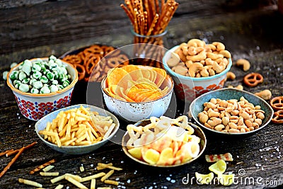 Different kinds of snacks - chips, salted peanuts, cashews, peas with wasabi, pretzels with salt, potatoes, salted straw. Stock Photo