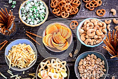 Different kinds of snacks - chips, salted peanuts, cashews, peas with wasabi, pretzels with salt, potatoes, salted straw. Stock Photo