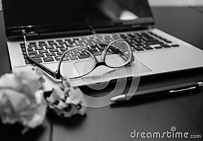 Different objects on black office desk. Modern black office desk table with laptop keyboard, pen, crumpled paper balls, glasses Editorial Stock Photo