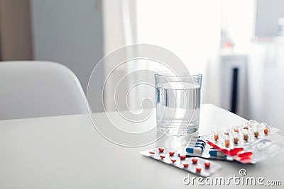 Different pills and glass of water on kitchen table. Healthcare and medicine Stock Photo